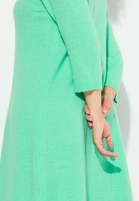 Abito maglione verde menta con maniche a tre quarti, texture morbida e silhouette svasata, con dettagli delle cuciture lungo il lato.