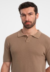 Brun kortärmad pikétröja av strukturerad stickad tyg. Har en klassisk krage och tvåknapps placket.