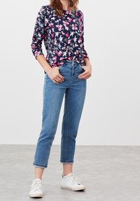 Květinová košile s dlouhým rukávem s růžovými a bílými květy na tmavě modrém pozadí, kombinovaná s světle modrými rovnými džíny a bílými teniskami.