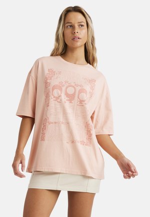 T-shirt oversize rose pâle à manches courtes, arborant un imprimé graphique détaillé en rose plus foncé, représentant trois phases de lune et des accents floraux.