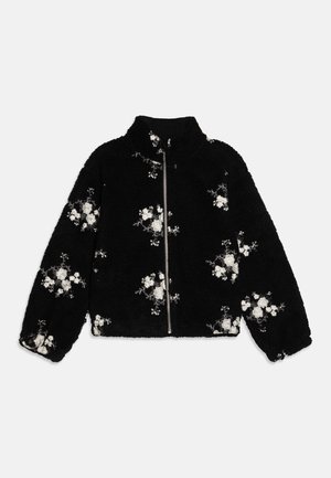 Black fleece jacket with high collar, zip closure, and floral embroidery in white. Features soft texture and loose fit, with ribbed cuffs.