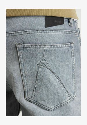 Heled sinine teksapüksid, millel on ainulaadne kolmekordne õmblusdisain taskutel, seljaosas musta nahast silt "CHASIN'".