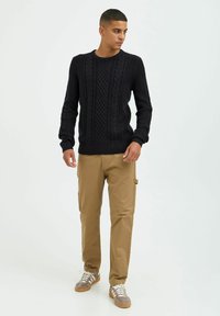 Marineblå strikkegenser med teksturerte detaljer, pairt med beige cargo-bukser. Antrekket inkluderer grå joggesko med hvite snøringer og brune detaljer.