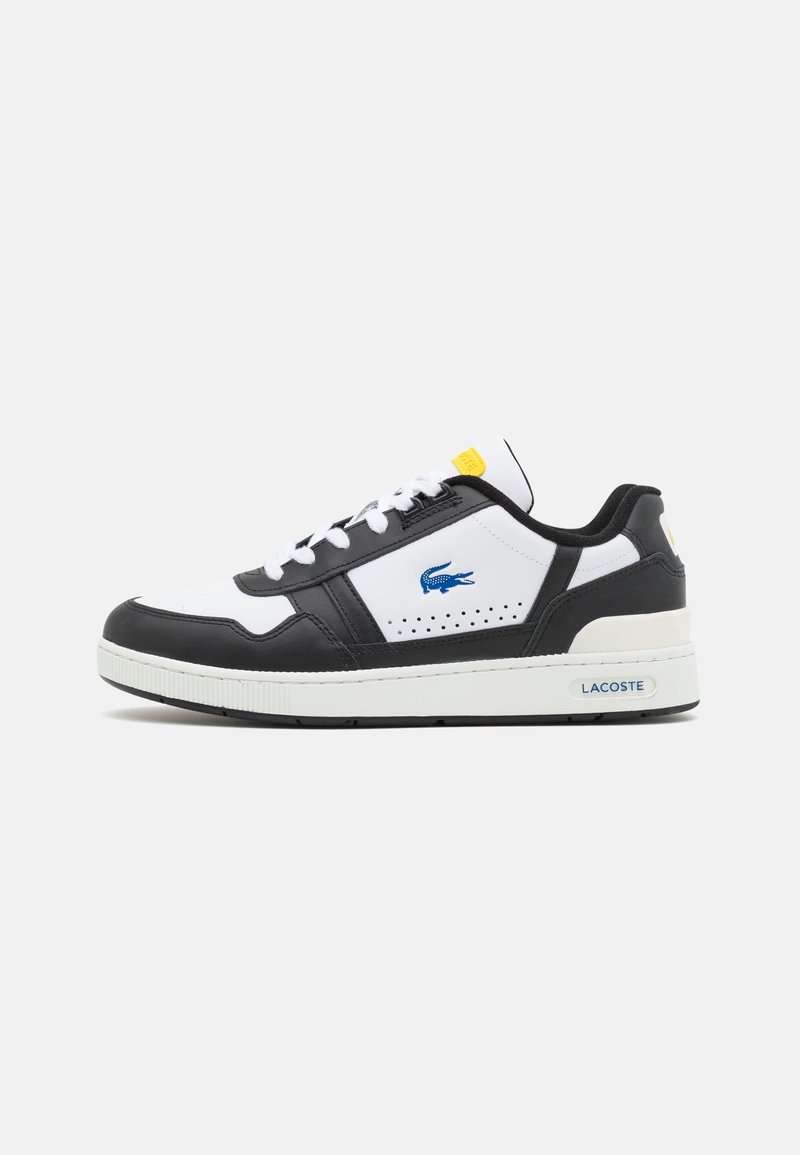 Baskets basses blanches et noires avec logo crocodile Lacoste bleu, lacets blancs et étiquette jaune sur la languette, marquage sur la semelle latérale sur fond uni.