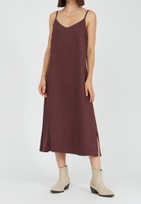 Mauve pitkähihaton maksimekko, jossa on V-pääntie, sivuaukot ja sileä kangas. Yhdistettynä kermaisiin nilkkabootseihin ja minimalistiseen muotoiluun.