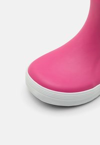 Botte en caoutchouc rose avec une surface lisse et un bout arrondi, dotée d'une semelle extérieure blanche à nervures et d'un design de talon légèrement surélevé.