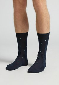 Calcetines azul marino con un puño acanalado, que presentan un patrón de pequeños cuadrados verdes. Fabricados con una tela suave y elástica para mayor comodidad.