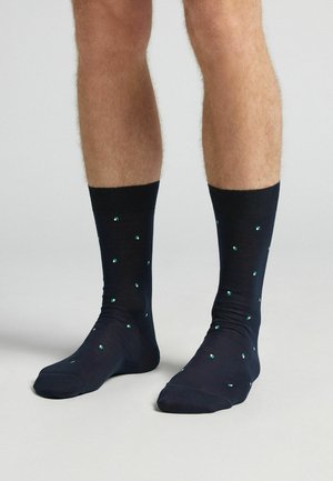 Calcetines azul marino con un puño acanalado, que presentan un patrón de pequeños cuadrados verdes. Fabricados con una tela suave y elástica para mayor comodidad.