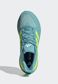 Zapatillas deportivas con parte superior en color teal, textura de malla, acentos en amarillo brillante y tres franjas blancas. Presentan cordones y un diseño acolchado.