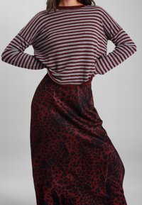 Maglietta a maniche lunghe a righe grigia e burgundy; abbinata a una gonna rosso scuro con motivo leopardato nero. Tessuto morbido, vestibilità rilassata.