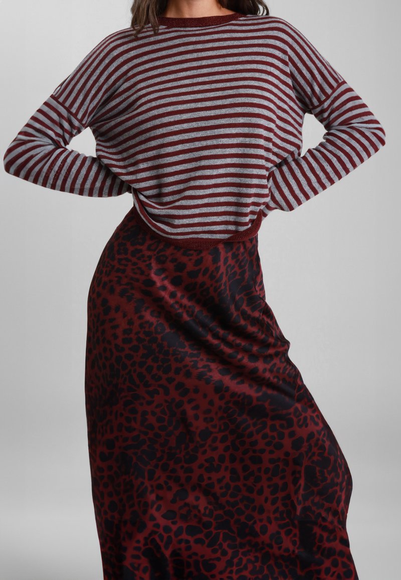 Maglietta a maniche lunghe a righe grigia e burgundy; abbinata a una gonna rosso scuro con motivo leopardato nero. Tessuto morbido, vestibilità rilassata.