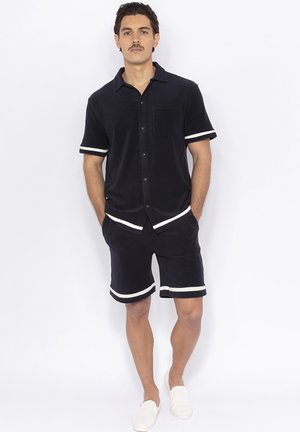 Marineblauwe badstof shirt met korte mouwen en witte details, voorzien van een borstzak, gecombineerd met bijpassende shorts met vergelijkbare witte accenten.