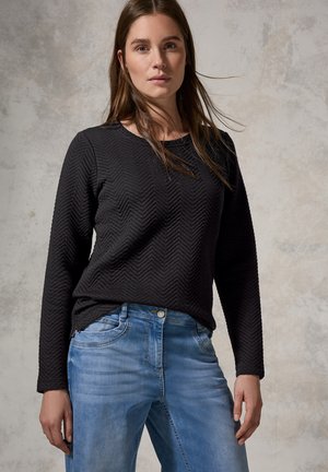 Zwarte longsleeve top met een chevrontextuur, gecombineerd met lichtblauwe spijkerbroek met een klassieke vijfzakkenontwerp en een knoopsluiting.