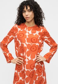 Φόρεμα με μακριά μανίκια και λουλουδάτο μοτίβο σε πορτοκαλί και λευκό. Το ύφασμα φαίνεται απαλό και ελαφρύ με στρογγυλή λαιμόκοψη.
