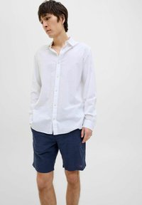 Witte blouse met lange mouwen en knopen, gemaakt van lichtgewicht stof, gecombineerd met marineblauwe shorts. Heeft een kraag en een subtiele textuur.