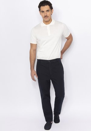 Polo-shirt blanc à col rabattu associé à un pantalon navy foncé et des chaussures décontractées, présentant une coupe slim et une texture lisse.