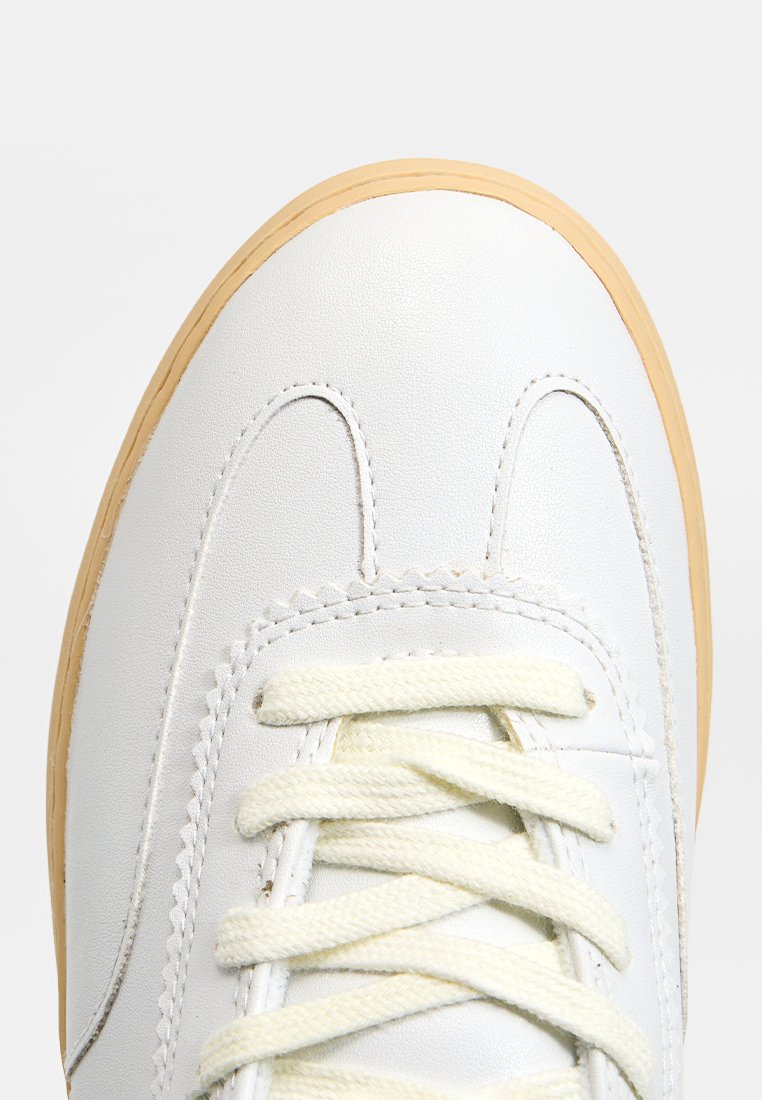 Sneaker en cuir blanc avec un bout arrondi, semelle en caoutchouc beige et lacets couleur crème. Couture détaillée le long de la tige.