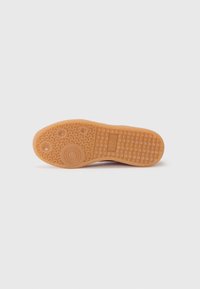 Semelle de chaussure en caoutchouc couleur beige clair, présentant une surface texturée avec des motifs circulaires et linéaires pour améliorer l'adhérence. Talon arrondi et avant plat.