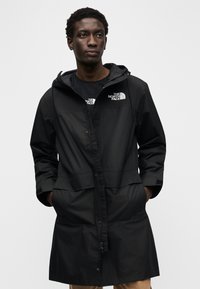 Μαύρο αδιάβροχο παρκά με κουκούλα, μπροστινό φερμουάρ, δύο μεγάλες τσέπες και το λογότυπο The North Face στο στήθος και το μανίκι.