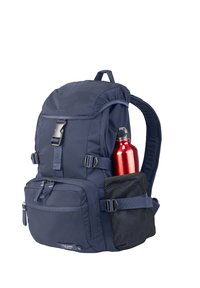 Zaino blu navy con tasca frontale, fibbia a cinturino, tasca laterale in rete contenente una bottiglia d'acqua metallica rossa e spallacci imbottiti.