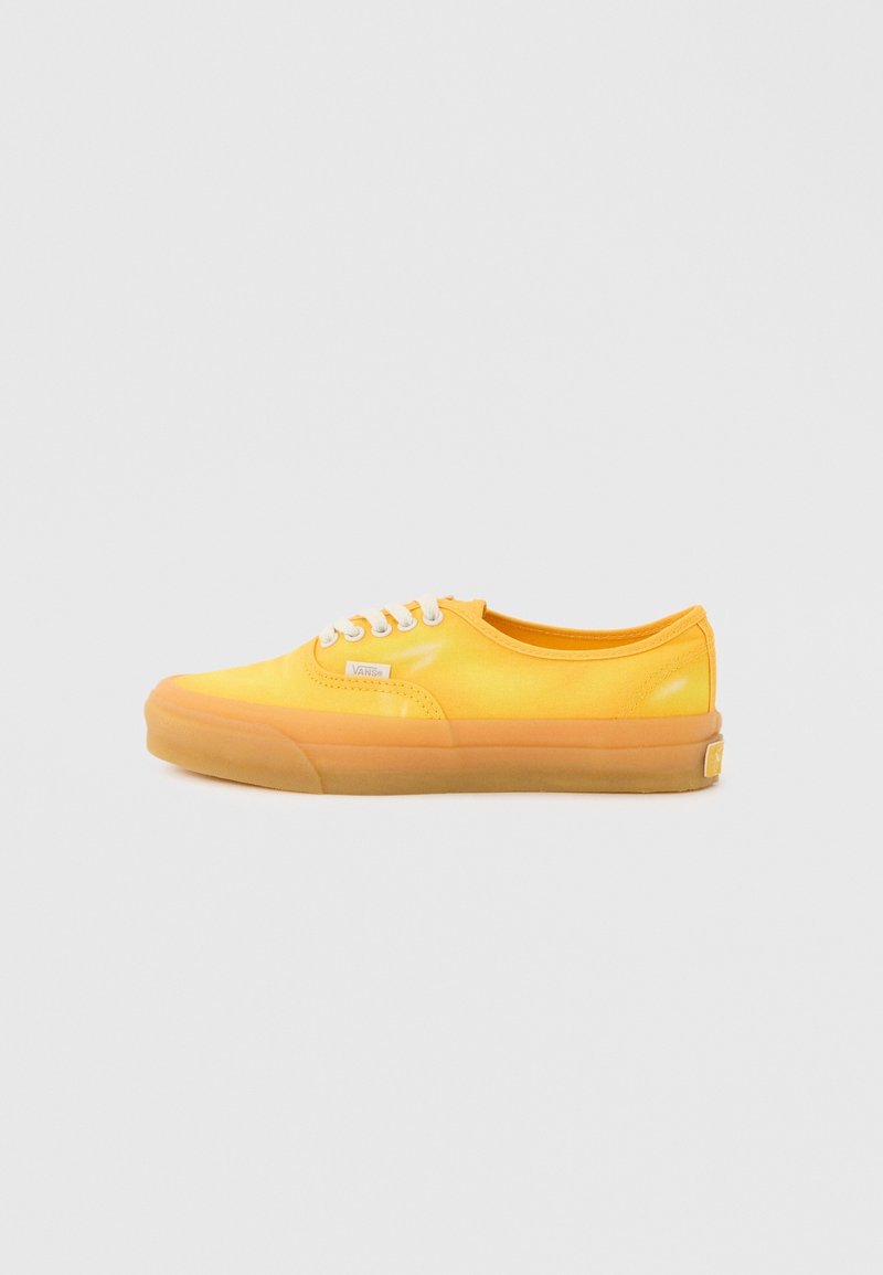 Baskets basses Vans jaunes avec des lacets blancs et une semelle en caoutchouc, vues de côté sur un fond gris clair.