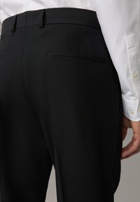 Pantaloni neri su misura con una texture liscia, dotati di una tasca posteriore singola e passanti per la cintura, abbinati a una camicia bianca.