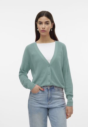 Cardigan verde menta con scollatura a V, testo a coste, tre bottoni e maniche lunghe, abbinato a jeans a vita alta blu chiaro.