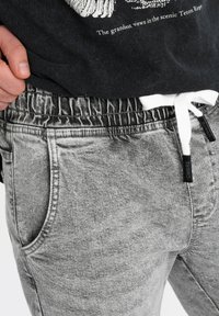 Jogging en gris avec cordon de serrage et coupe décontractée. Doté d'un tissu texturé, d'une taille élastique et d'un cordon de serrage blanc contrastant.