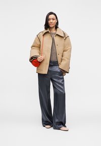 Μπεζ μπουφάν με ραφές και μαύρο περίγραμμα, γκρι πουλόβερ και μπλε σατέν παντελόνι φαρδιάς γραμμής. Κρατά μικρή κόκκινη τσάντα· ολοκληρώνει την εμφάνιση με ανοιχτόχρωμα παπούτσια.