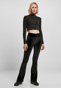 Musta, lyhyt pitkähihainen paita yhdistettynä istuviin, hieman levenevin mustiin samettihousuihin. Asussa on sileä tekstuuri ja minimalistinen muotoilu.