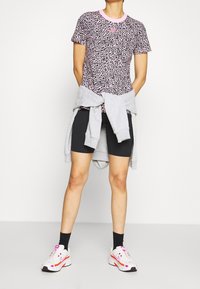 Leopardmönstrad kortärmad skjorta med rosa detaljer, tillsammans med svarta cykelshorts och en grå sweatshirt knuten i midjan. Vita sneakers med rosa detaljer.