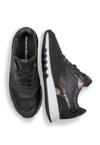 Scarpe sportive nere con una combinazione di camoscio e accenti metallici, pannelli laterali testurizzati e un design di suola bianca a zigzag.