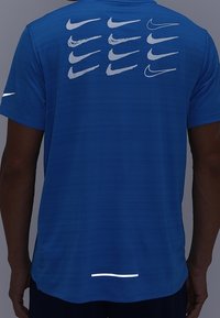 Blauwe Nike sportshirt met meerdere witte logo-afdrukken op de achterkant. Korte mouwen, lichtgewicht stof, met een reflecterende accent aan de zoom.