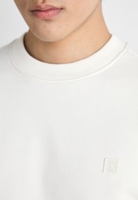 Λευκή βαμβακερή μπλούζα με ριμπ λαιμόκοψη και μικρό κεντημένο λογότυπο στη πάνω αριστερή γωνία. Λείος υφασμάτινος τύπος, casual σχεδίαση.