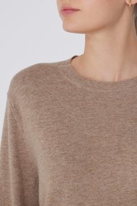 Beżowy sweter wełniany z okrągłym dekoltem, o miękkiej fakturze i ściągaczach na rękawach. Posiada subtelny melanżowy wzór.