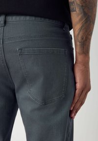 Vaqueros de mezclilla gris oscuro con un diseño ajustado, que cuentan con un solo bolsillo trasero y detalles de costura sutiles. Textura suave y líneas limpias.