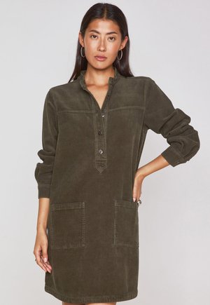 Olijfgroene corduroy jurk met een kraag, knoopsluiting en twee voorzakken. Lange mouwen met manchetten en een geweven, ribbelstof.