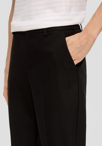 Pantalon noir avec une texture lisse, doté d'une poche latérale, au design slim fit, et avec un pli subtil à l'avant.