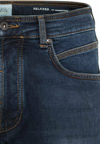 Luźno krojone ciemnoniebieskie dżinsy z pomarańczowym przeszyciem, z zapięciem na guzik i kieszenią z przodu. Powierzchnia materiału wydaje się gładka i mocna.