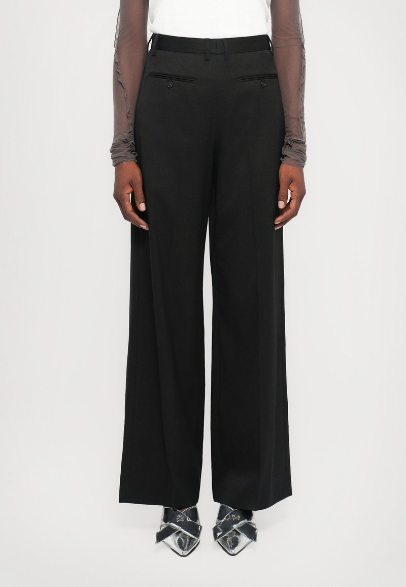 Black wide-leg trousers with a smooth texture, featuring front pockets and subtle detailing. Paired with pointed silver shoes for contrast.