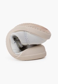 Weiße, weiche Schuhe aus flexiblem Material, runde Form, strukturierte beige Sohle und dezente Nähdetails. Lassen sich in die Lagerposition zusammenfalten.
