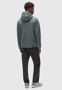 Grau Hoodie mit strukturierter Stoffqualität, locker geschnitten. Kombiniert mit dunklen Jeans und Sportschuhen in neutraler Farbe.