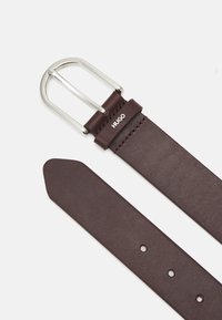 Cintura in pelle marrone con una fibbia metallica argentata, dotata di un accento logo e numerosi fori di regolazione lungo la cinghia per la variabilità delle misure.