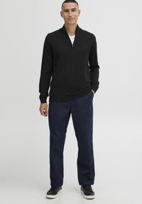 Black zip-neck sweater made of knit fabric, paired with navy blue straight-leg trousers and black leather sneakers. Simple design, no notable patterns.