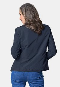 Marineblau leichte Jacke mit langen Ärmeln, glatter Textur und einfachem Design, kombiniert mit blauen Jeans. Sichtbare Nähtte an den Ärmeln.