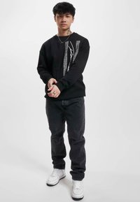Black sweatshirt with white graphic design and text on the front, paired with dark jeans and white sneakers. Simple, casual outfit.