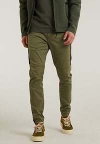 Olive green slim-fit pants with black side panels, a smooth texture, and knee stitching detail, complemented by lace-up green sneakers.