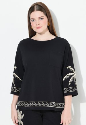 Chemise noire en coton à manches trois quarts, avec des broderies blanches de palmiers et de vagues le long des manches et de l'ourlet, plus une poche avant.