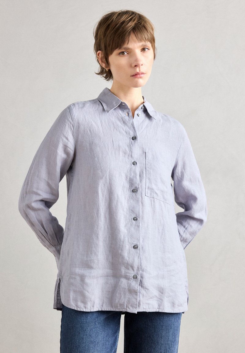Light gray linen shirt with a collar, long sleeves, front pocket, and button closure; smooth texture with side slits at the hem.