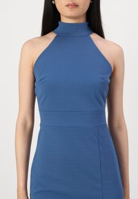 Rochie albastră cu guler halter, cu un corset ajustat și textură fină. Prezintă un guler înalt și detalii subtile ale cusăturii la talie.